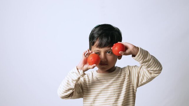 Indian boy holding fresh tomatoes. Child playing with healthy vegetables in studio.