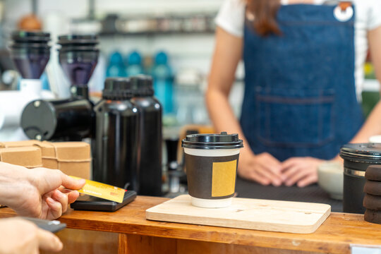 Credit card payment at coffee shop counter. Cafe owner using card reader for cashless transaction while serving coffee drink to customer. Electronic payment technology for small business retail store.