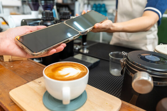Title: Cashless mobile payment at coffee shop counter, customer and barista using smartphones mobile app for contactless digital electronic banking transaction while buying hot coffee at small busines