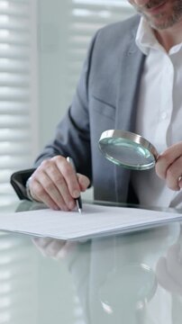 Mature man in suit carefully examining business document with a magnifying glass, analyzing contract details and terms for legal compliance or financial scrutiny