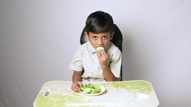 Indian boy eating fresh green salad. Healthy child having vegetable meal at home.