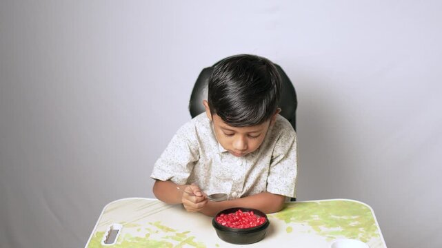 Indian boy eating pomegranate seeds. Healthy child having fresh fruit snack at home.