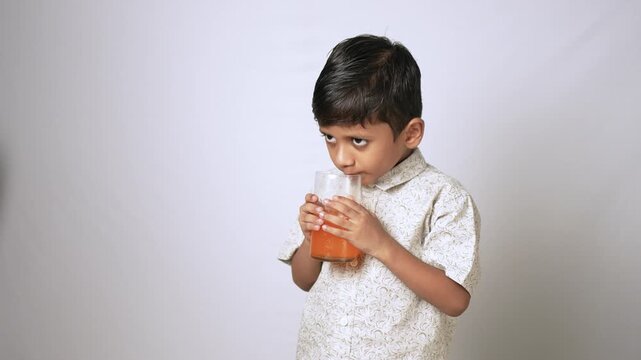 Indian boy drinking orange juice. Child holding a glass of fresh fruit beverage.