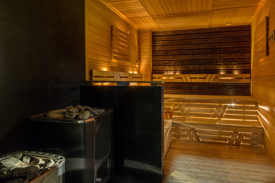 A sauna room shows wooden benches and a heater with stones ready for heating. The warm lighting creates a cozy atmosphere for relaxation 