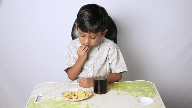 Indian boy eating snacks at home. Young child enjoying crispy chips and cold drink.