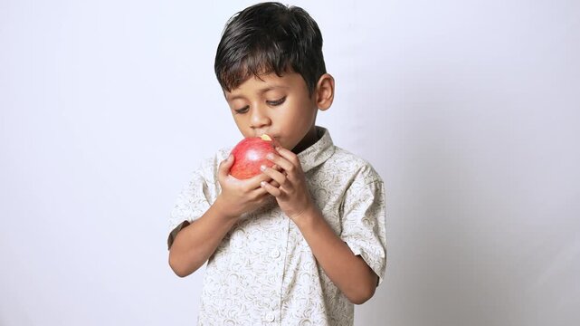 Indian boy eating a fresh red apple. Healthy child enjoying organic fruit snack.