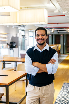 Confident young man with crossed arms smiling at camera. Representing professionalism, collaboration, and success in a contemporary office