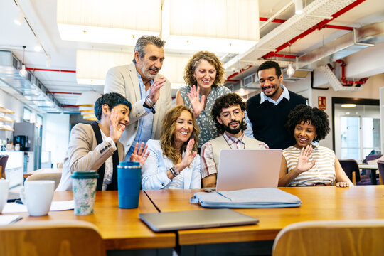 Happy business people video conferencing on laptop, collaborating and communicating in a modern shared office environment