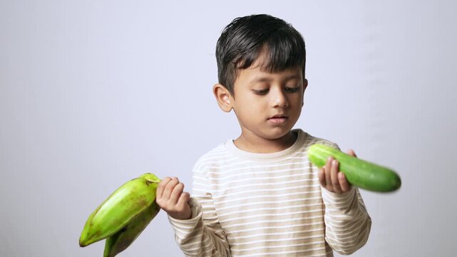 Indian boy eating fresh cucumber. Healthy child snacking on raw organic vegetables.