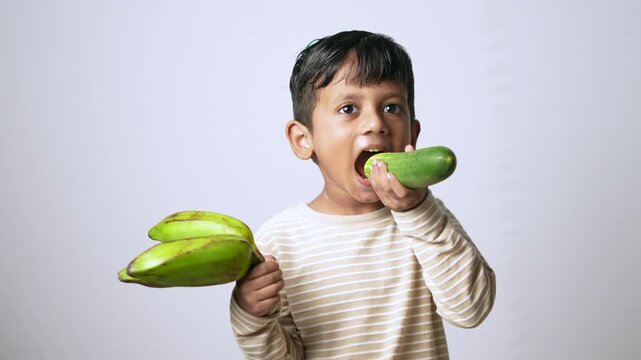 Indian boy eating fresh cucumber. Healthy child snacking on raw organic vegetables.