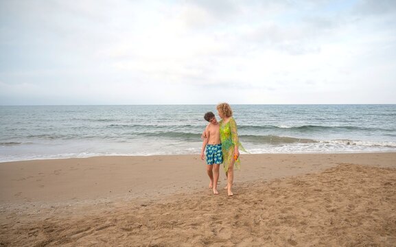 Mother and teenager walking arm in arm along the beach while enjoying a peaceful summer day by the sea