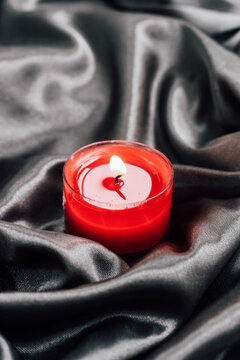 Red candle on black silk fabric with a flickering flame in a dimly lit setting
