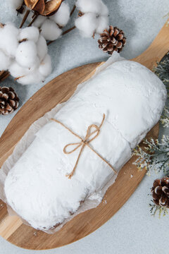 Freshly made Christmas stollen resting on a wooden board with pinecones and cotton decorations on a table