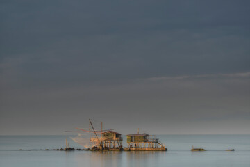 Rustic wooden fishing huts standing in still water under a dramatic overcast sky. Ideal for travel and heritage themes. © marcodenaro