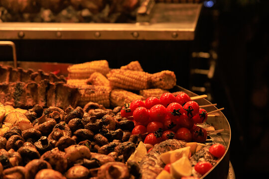 Food being prepared at a market with various meats vegetables and corn displayed on skewers and platters