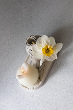 Candle and narcissus flower arrangement on a light surface with soft lighting in a simple setting