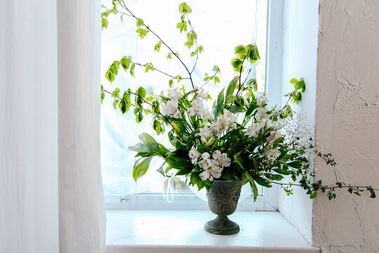 Fresh alstroemeria flowers in a vase placed on a white windowsill with sunlight shining through the window in a bright room