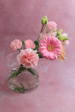Bright pink flowers in a clear glass vase on a light pink background in a simple arrangement