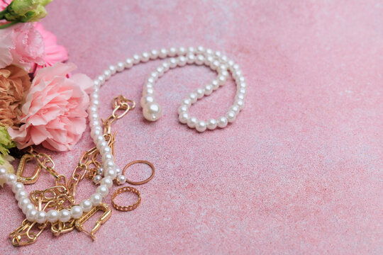 Jewelry laid out on a pink surface with flowers and decorative elements present in an indoor setting during daylight