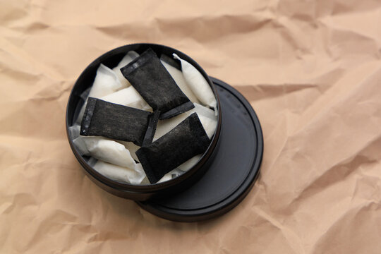 Snus pouches in a round tin container on brown paper background with several pouches visible from above