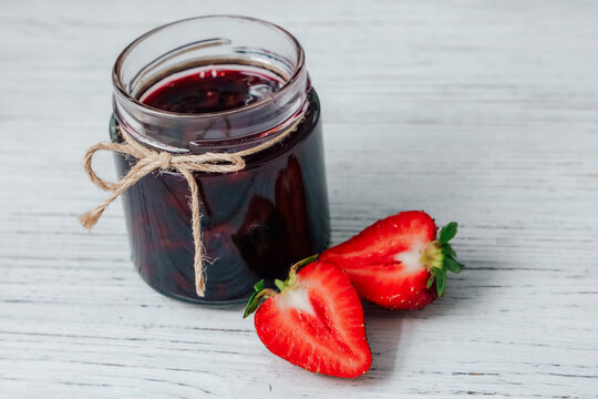 Fresh strawberries and jar of homemade jam on wooden table in kitchen setting during afternoon light