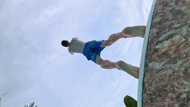 Young man performs impressive backflip into a sparkling blue swimming pool