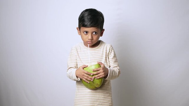 Indian boy drinking fresh coconut water. Child enjoying healthy natural drink in studio.