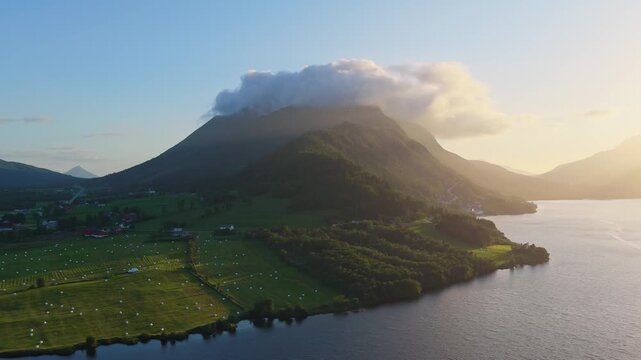 Aerial drone view of a fjord and mountains at sunset in Norway. Sunset glow on sky and clouds over mountain peaks during summer travel.
