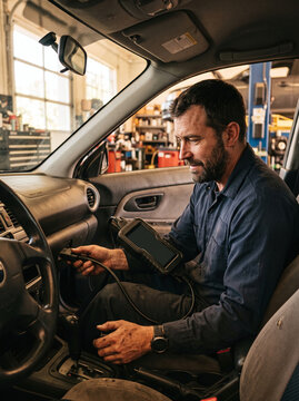 Professional mechanic using OBD diagnostic scanner tool inside car at garage