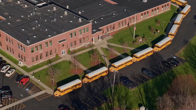 Drone view of yellow school buses lined up outside an American school building in autumn