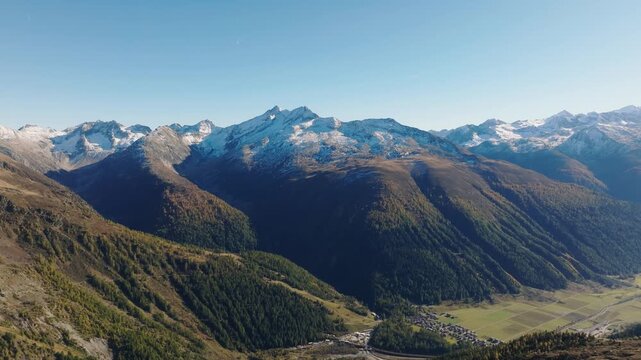 Aerial drone view of a mountain valley with dense forest surrounded by high alpine peaks. Travel and nature landscape concept.