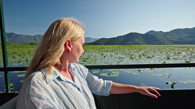 Middle aged woman enjoying a peaceful boat trip across Skadar Lake National Park in Montenegro. She admires water lilies and mountain landscapes 