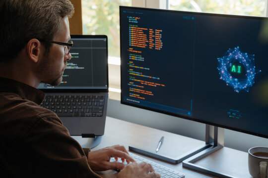 Focused coder using AI assistant to write programing code on computer at desk with dual screens, boosting productivity and automation with artificial intelligence agents and AI chatbots. Copy space