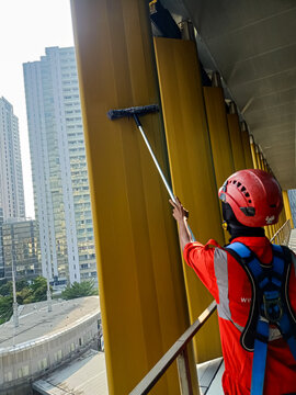 Professional cleaner using extension pole to clean yellow architectural panels of modern skyscraper
