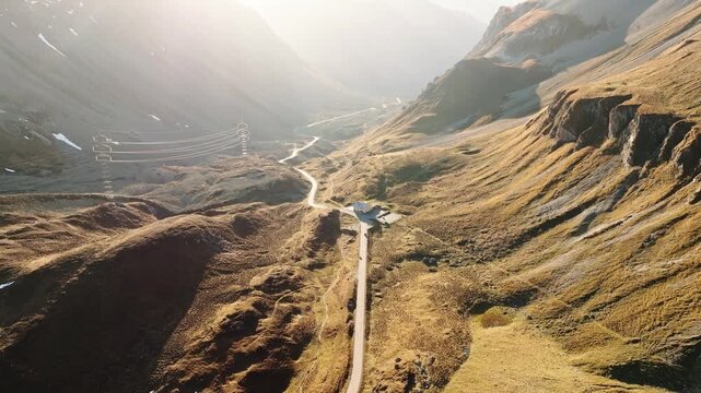 Aerial drone view of a winding road in a mountain valley during a golden sunset glow. Transportation and travel concept.