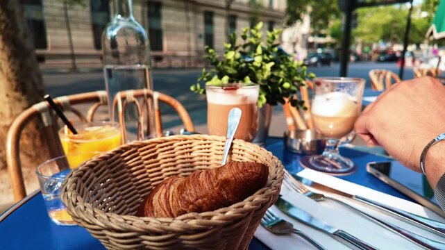 A delicious breakfast of coffee and a croissant sits on a table in front of a busy city street with a double-decker bus