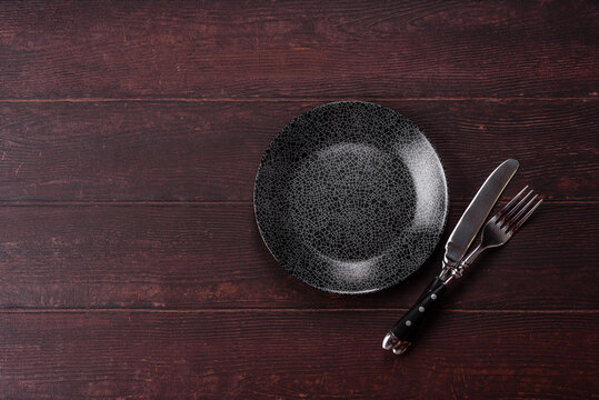 An empty round ceramic plate on a dark, textured brown background. An empty round plate