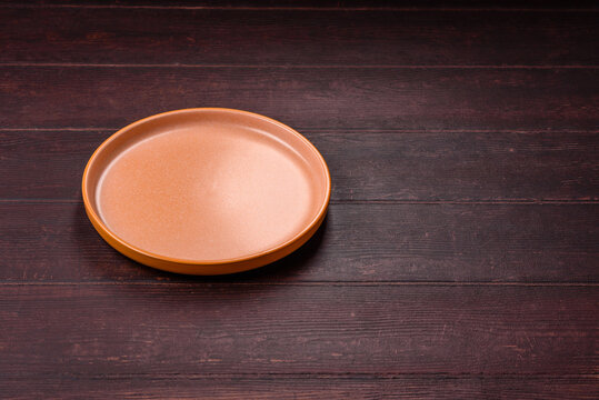 An empty round ceramic plate on a dark, textured brown background. An empty round plate