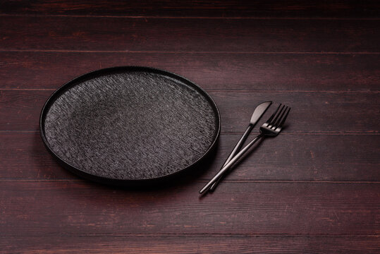 An empty round ceramic plate on a dark, textured brown background. An empty round plate