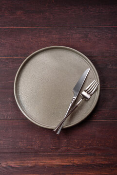 An empty round ceramic plate on a dark, textured brown background. An empty round plate