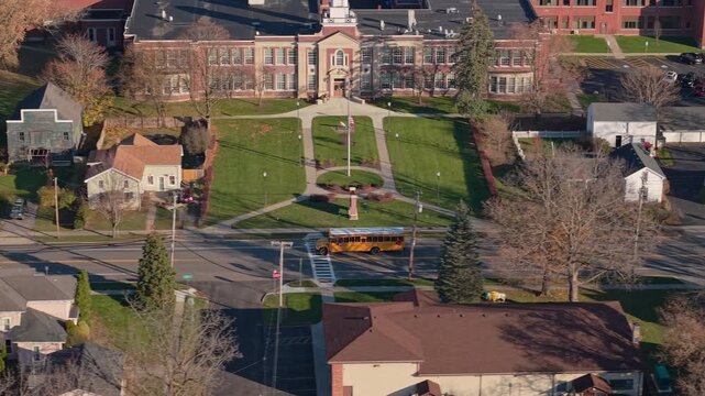 Yellow school bus driving past an American school campus in a suburban neighborhood
