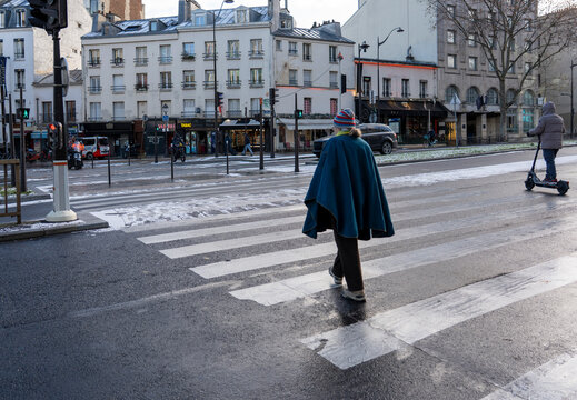 Woman crossing a pedestrian crossing after light snowfall in Paris during winter with wet streets and cold weather in the French capital