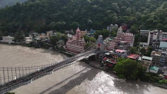 Aerial drone footage of Rishikesh during monsoon, showcasing the Ganges River, Ram Jhula, Lakshman Jhula, lush green Himalayan foothills, temples, and the scenic spiritual city of Uttarakhand.