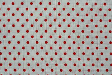 Textured knit fabric displaying a repeating pattern of small red polka dots on a white background © Floren Horcajo