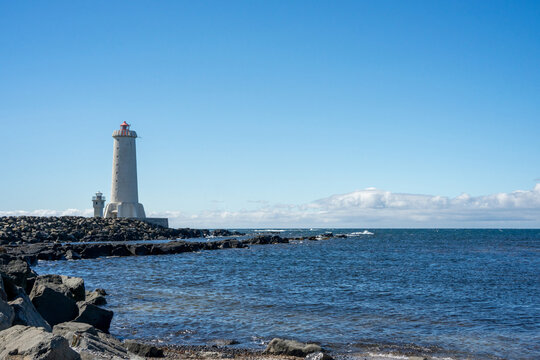 Two scenic concrete lighthouses on the rocky coast of Akranes, Iceland under a blue sky.