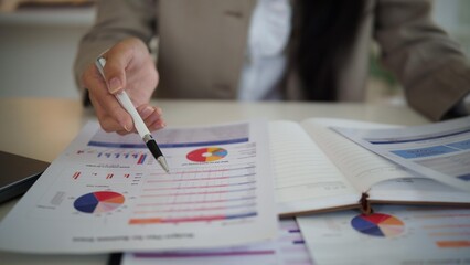Close up of businesswoman reviewing financial documents with pen, notebook, and business graphs on...