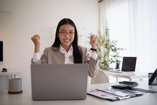 Excited businesswoman celebrating success while working on laptop in a bright modern office.