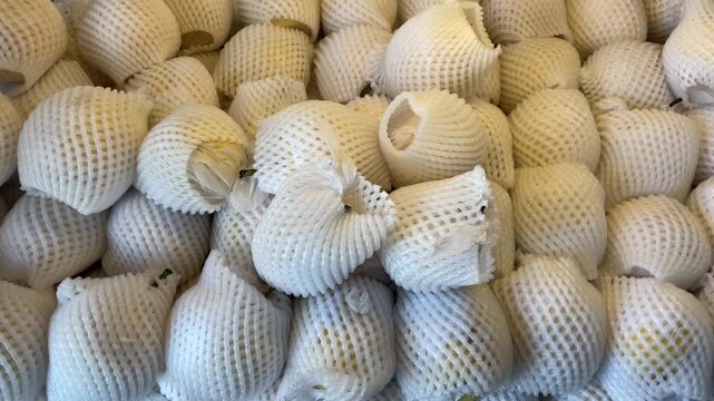 A stack of pears in white, perforated foam packaging at a fresh fruit vendor's stall.