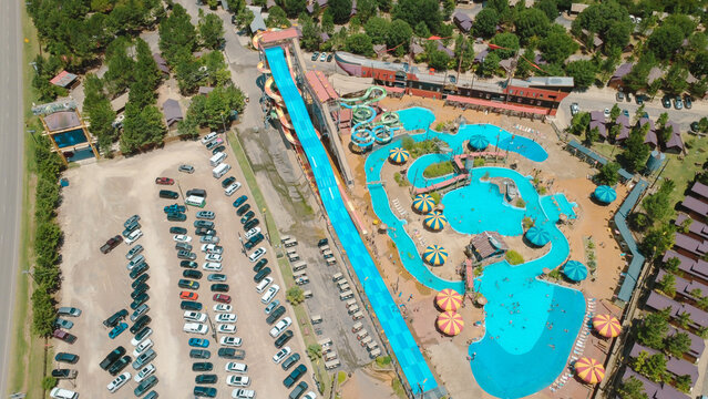 Water park facilities near Fort Worth feature mat slides. Swimming pools, pirate ship structures, parking lots illustrate popular resort features bathed in warm sunny summer light, Burleson, TX