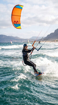 Happy female kitesurfer riding waves with scenic mountains in the background